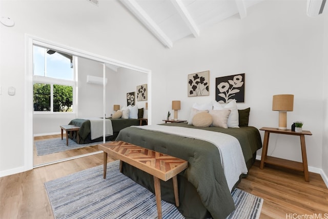 bedroom featuring vaulted ceiling with beams, light wood-type flooring, a wall mounted AC, and a closet