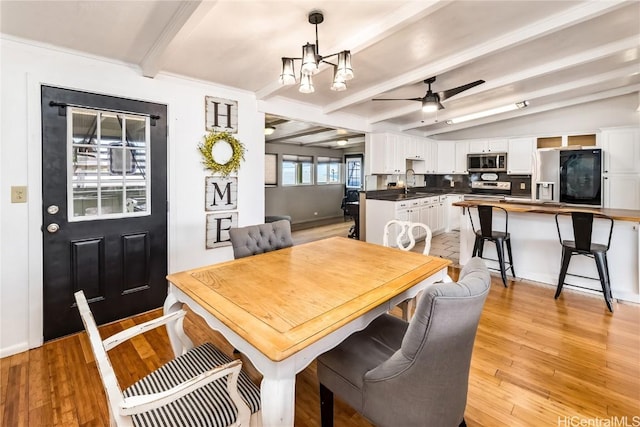 dining area with vaulted ceiling with beams, ceiling fan with notable chandelier, sink, and light hardwood / wood-style flooring