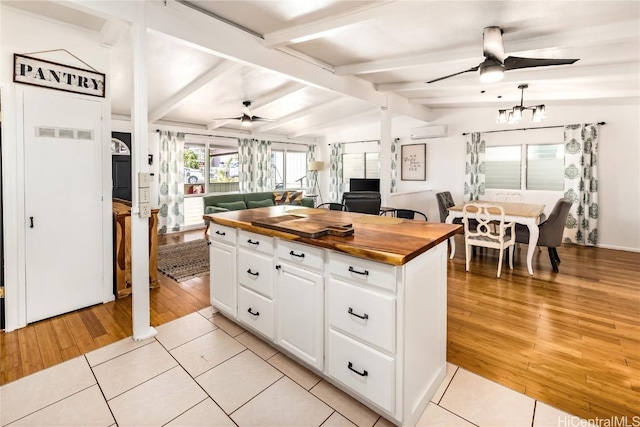 kitchen with wood counters, vaulted ceiling with beams, light tile patterned floors, a wall mounted AC, and white cabinetry