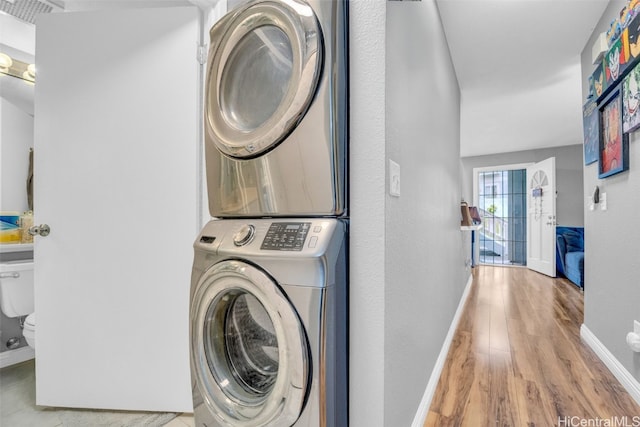 clothes washing area with stacked washing maching and dryer and light hardwood / wood-style floors