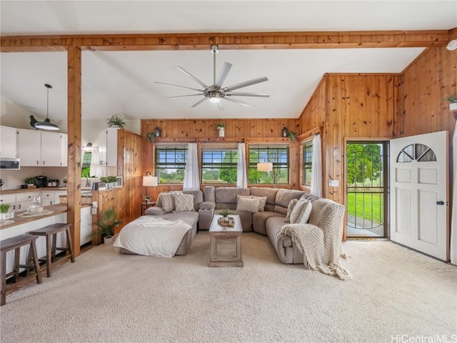 carpeted living room featuring wood walls, vaulted ceiling with beams, and ceiling fan