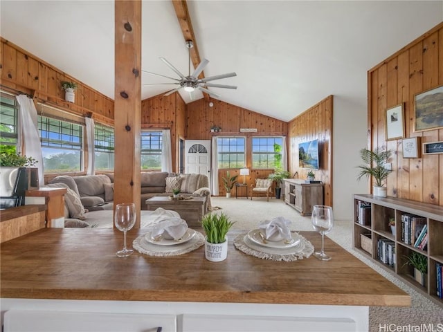 dining space with carpet floors, lofted ceiling with beams, ceiling fan, and wood walls