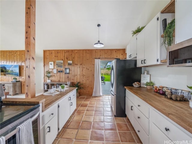 kitchen featuring butcher block counters, decorative light fixtures, wooden walls, white cabinets, and appliances with stainless steel finishes