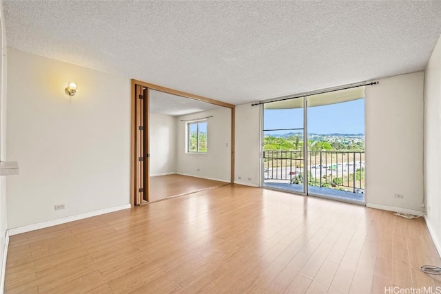 empty room with floor to ceiling windows, a textured ceiling, and light wood-type flooring