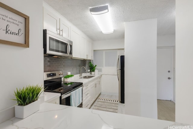 kitchen with backsplash, sink, light stone counters, white cabinetry, and stainless steel appliances