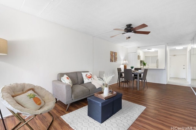 living room with a textured ceiling, ceiling fan, and dark wood-type flooring