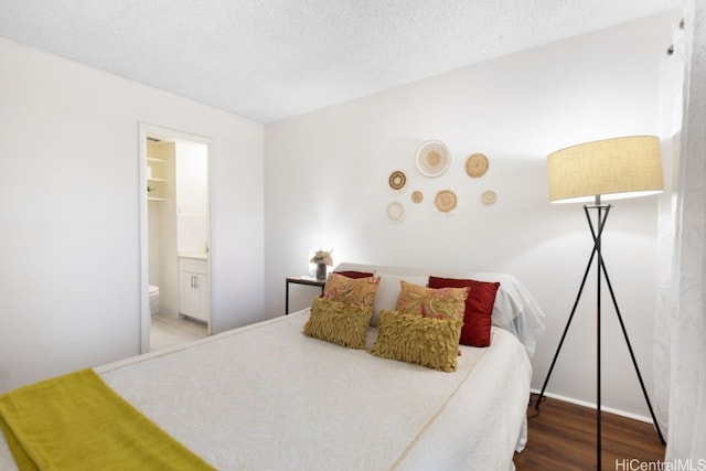 bedroom with connected bathroom, hardwood / wood-style floors, and a textured ceiling