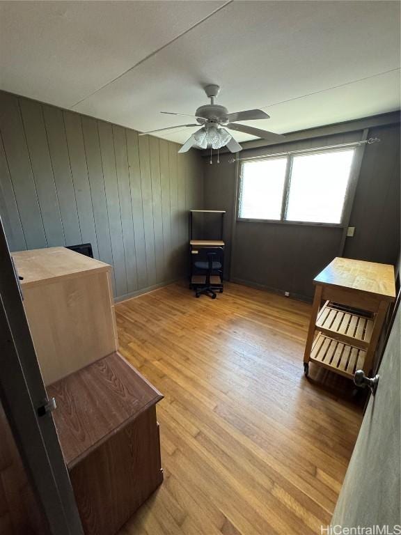 interior space with ceiling fan, wood walls, and light wood-type flooring