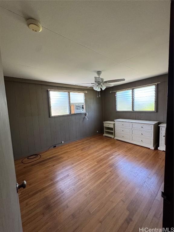 unfurnished bedroom featuring ceiling fan, wooden walls, and light wood-type flooring