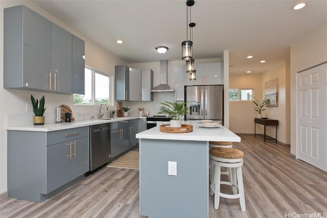 kitchen featuring appliances with stainless steel finishes, sink, wall chimney range hood, pendant lighting, and a center island