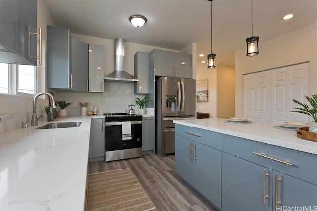 kitchen with stainless steel appliances, sink, wall chimney range hood, decorative light fixtures, and dark hardwood / wood-style floors