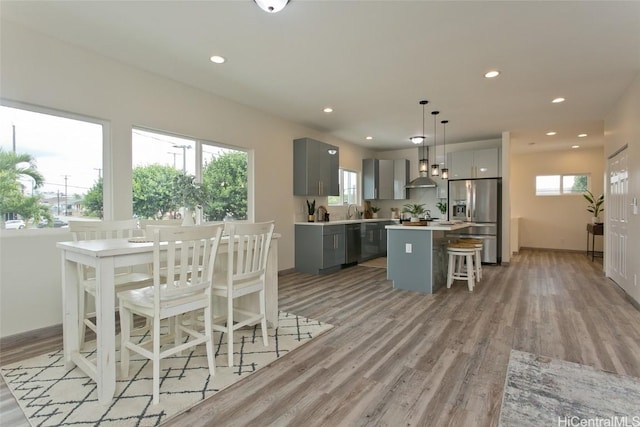 kitchen with gray cabinetry, a center island, wall chimney range hood, decorative light fixtures, and stainless steel fridge with ice dispenser