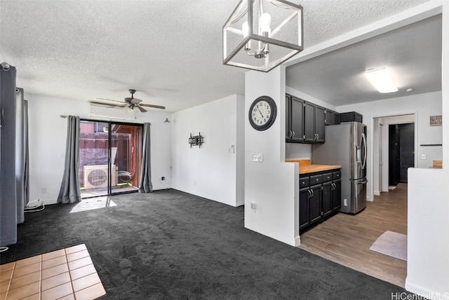 kitchen with dark colored carpet, ceiling fan with notable chandelier, stainless steel fridge, a textured ceiling, and decorative light fixtures