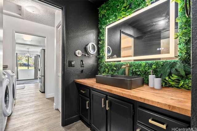 bathroom with vanity, a textured ceiling, separate washer and dryer, an inviting chandelier, and hardwood / wood-style flooring