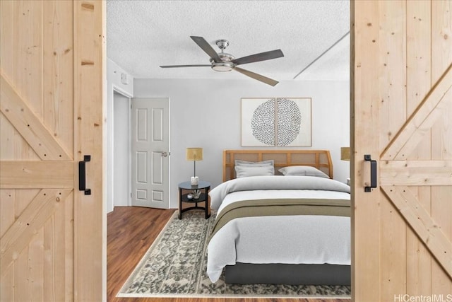 bedroom with ceiling fan, a barn door, wood-type flooring, and a textured ceiling