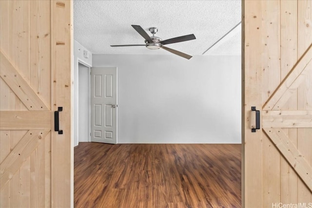 spare room featuring a textured ceiling, a barn door, hardwood / wood-style flooring, and ceiling fan