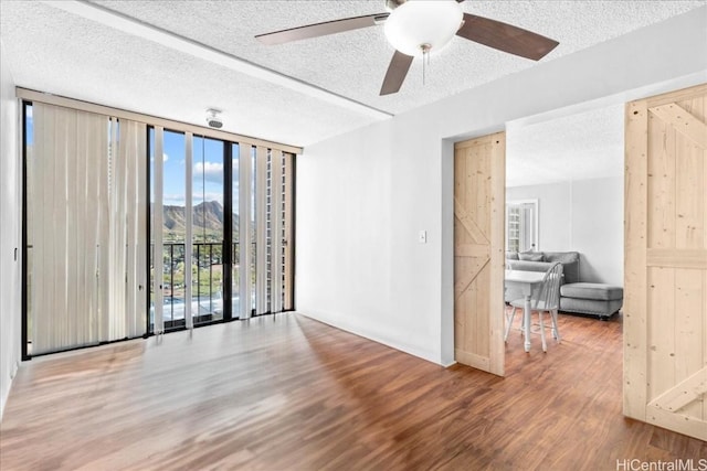 spare room with expansive windows, a textured ceiling, ceiling fan, a barn door, and hardwood / wood-style floors