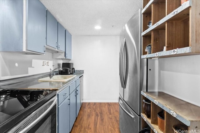 kitchen featuring appliances with stainless steel finishes, a textured ceiling, blue cabinets, dark wood-type flooring, and sink