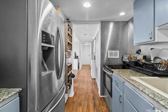 kitchen with a textured ceiling, dark hardwood / wood-style floors, blue cabinetry, and appliances with stainless steel finishes