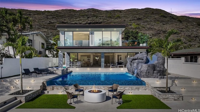 back house at dusk with a patio area, pool water feature, an outdoor fire pit, a mountain view, and a fenced in pool