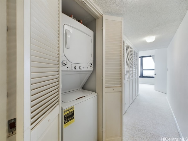 laundry area with stacked washer / drying machine, light colored carpet, and a textured ceiling