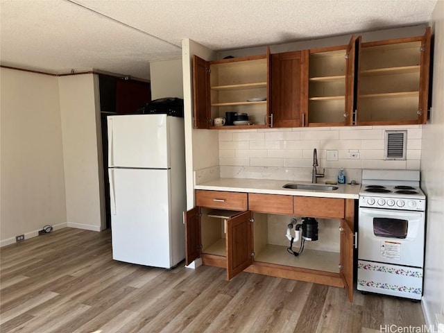 kitchen with decorative backsplash, light wood-type flooring, a textured ceiling, white appliances, and sink