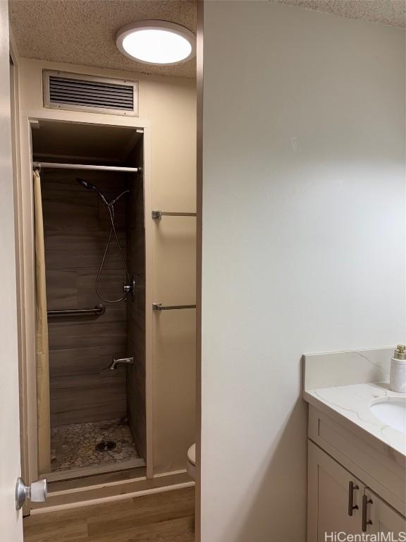 bathroom featuring hardwood / wood-style flooring, vanity, a textured ceiling, and walk in shower