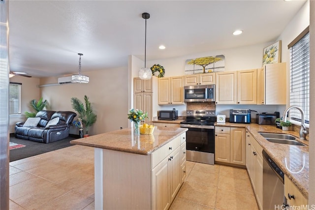 kitchen with light stone countertops, appliances with stainless steel finishes, sink, a kitchen island, and hanging light fixtures