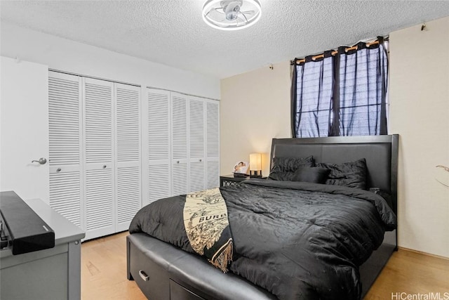 bedroom with a textured ceiling, light hardwood / wood-style flooring, and multiple closets