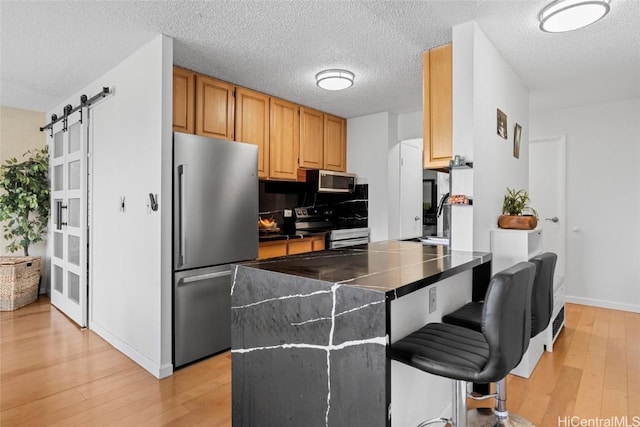 kitchen featuring a breakfast bar, a barn door, a textured ceiling, light brown cabinetry, and appliances with stainless steel finishes