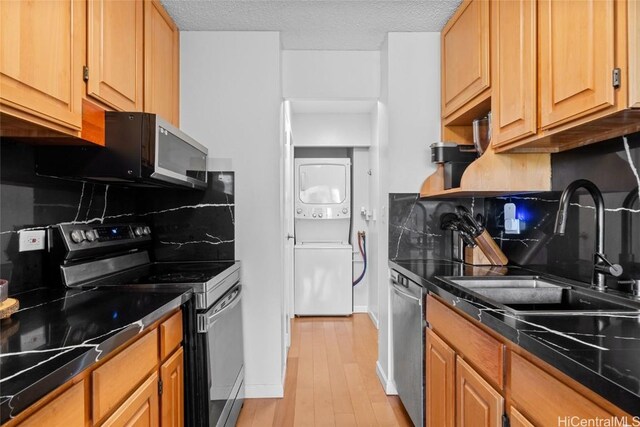 kitchen with sink, stacked washer and dryer, light hardwood / wood-style flooring, a textured ceiling, and stainless steel appliances