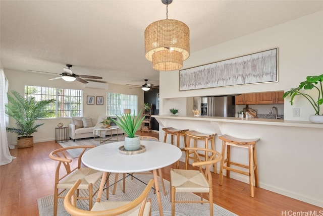 dining room with light wood-type flooring, ceiling fan with notable chandelier, an AC wall unit, and sink