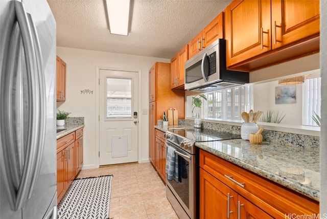 kitchen featuring a textured ceiling, stainless steel appliances, a healthy amount of sunlight, and light stone countertops