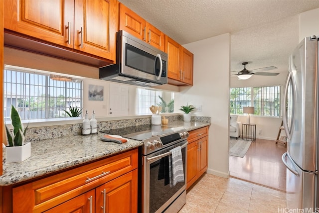 kitchen featuring light stone countertops, a textured ceiling, appliances with stainless steel finishes, ceiling fan, and light tile patterned floors