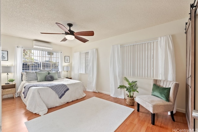 bedroom with ceiling fan, a textured ceiling, wood-type flooring, and an AC wall unit