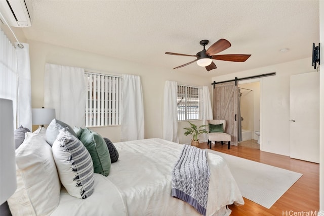 bedroom featuring a barn door, hardwood / wood-style floors, ceiling fan, a wall mounted air conditioner, and a textured ceiling