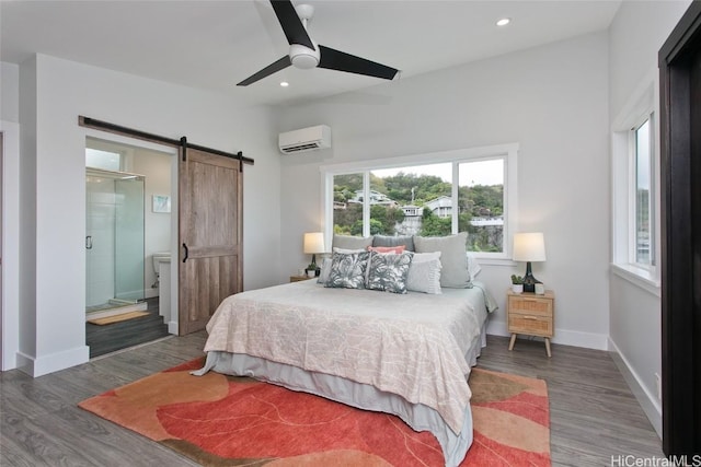 bedroom featuring ensuite bathroom, a barn door, ceiling fan, a wall mounted air conditioner, and dark hardwood / wood-style flooring