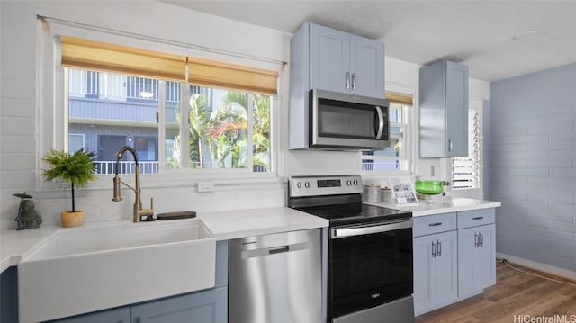 kitchen with sink, stainless steel appliances, brick wall, and wood-type flooring