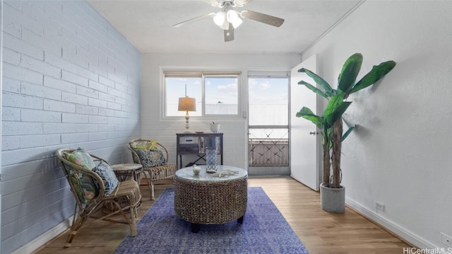 living area with ceiling fan, brick wall, and light hardwood / wood-style flooring