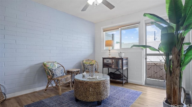 living area featuring ceiling fan, brick wall, and light hardwood / wood-style flooring