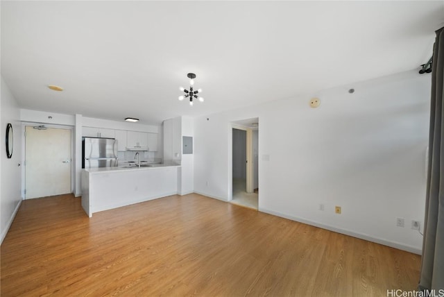 unfurnished living room featuring light hardwood / wood-style floors, sink, and an inviting chandelier