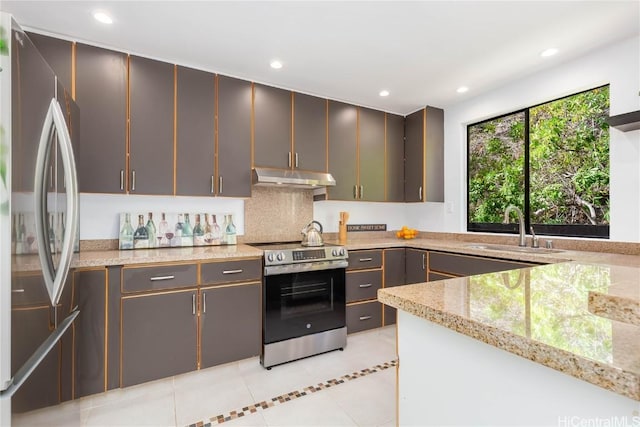 kitchen with appliances with stainless steel finishes, sink, light stone counters, light tile patterned flooring, and decorative backsplash