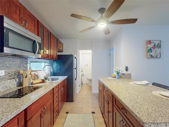 kitchen with appliances with stainless steel finishes, backsplash, light stone counters, ceiling fan, and sink