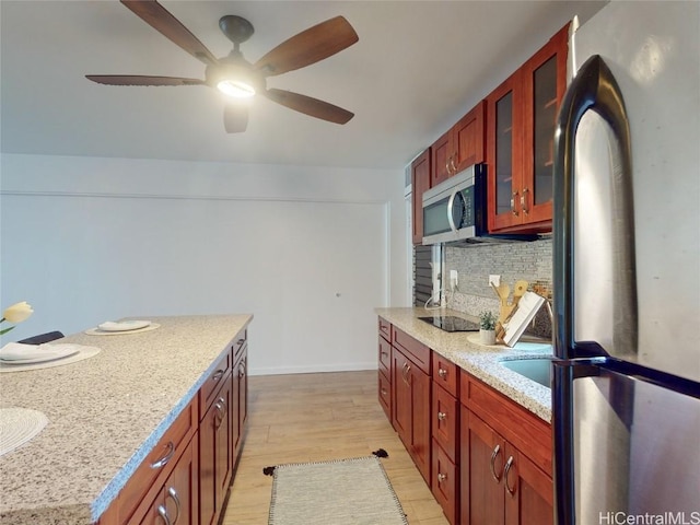 kitchen with appliances with stainless steel finishes, light wood-type flooring, backsplash, light stone counters, and ceiling fan