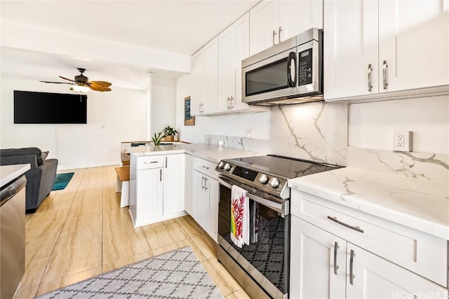 kitchen featuring light stone countertops, white cabinetry, ceiling fan, stainless steel appliances, and kitchen peninsula