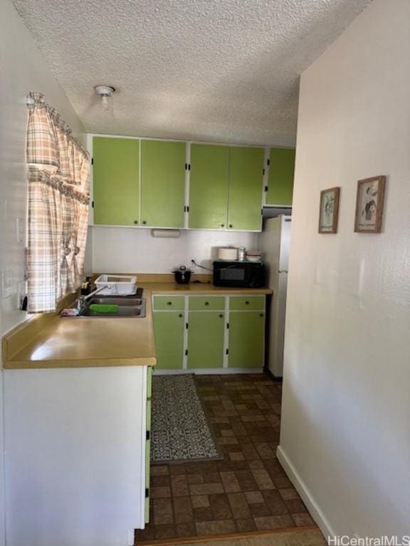 kitchen with a textured ceiling, refrigerator, sink, and green cabinetry