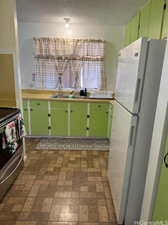 kitchen featuring white refrigerator, green cabinets, a textured ceiling, and stainless steel range oven