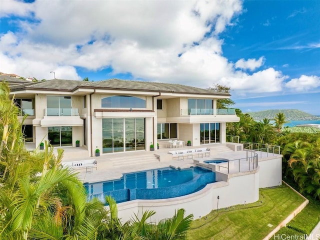 back of house with a balcony, a patio area, and a pool with hot tub