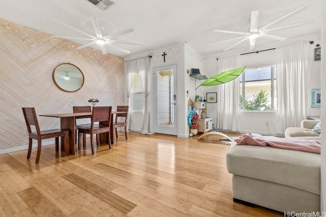 living room featuring wooden walls, ceiling fan, and light hardwood / wood-style floors