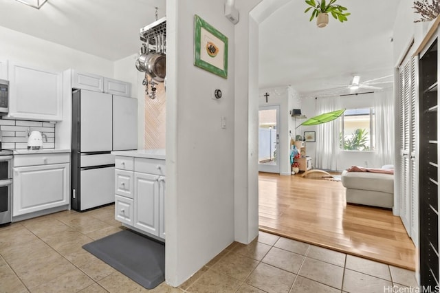 kitchen featuring ceiling fan, light tile patterned floors, backsplash, white cabinets, and appliances with stainless steel finishes